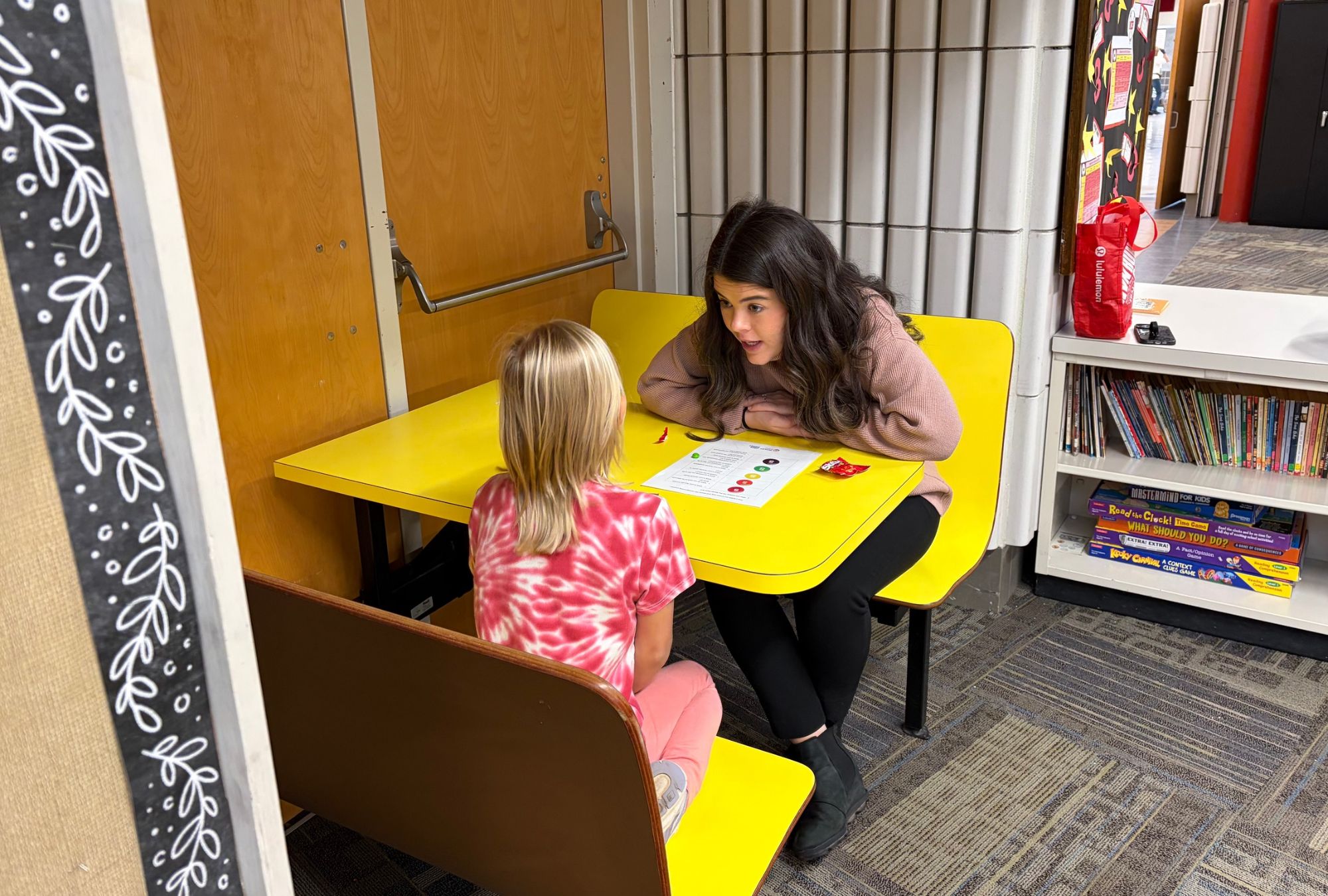 Lunch Buddies mentor and mentee play a game at a yellow table.