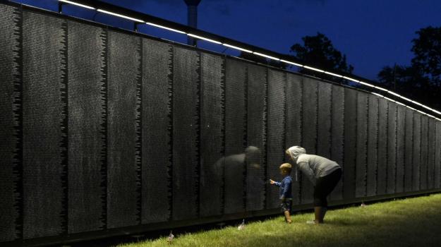 A woman and small child look at The Wall That Heals Vietnam Veterans Memorial replica in Chisholm. The sky is dark, but The Wall is illuminated. Photo by Dennis Barry.