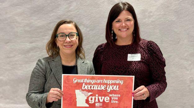 Department of Iron Range Resources and Rehabilitation Commissioner Ida Rukavina (left) and United Way of Northeastern Minnesota (UWNEMN) Executive Director Erin Shay hold a sign that says "Great things are happening because you Give Where You Live!"