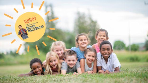 Children lie in grass in park, smiling. In top left corner, a sun graphic with the Buddy Backpacks logo inside