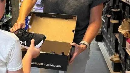 A volunteer hands new shoes to a child to try on during UWNEMN's Step Into School program